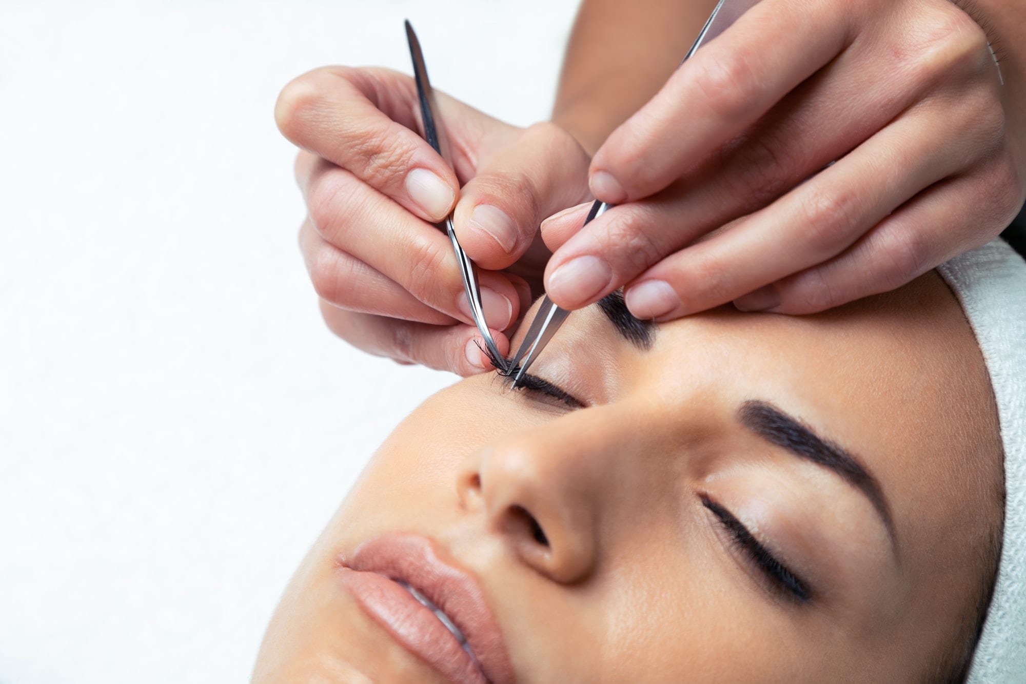 Cosmetologist doing the eyelash extension procedure on a woman over white background.