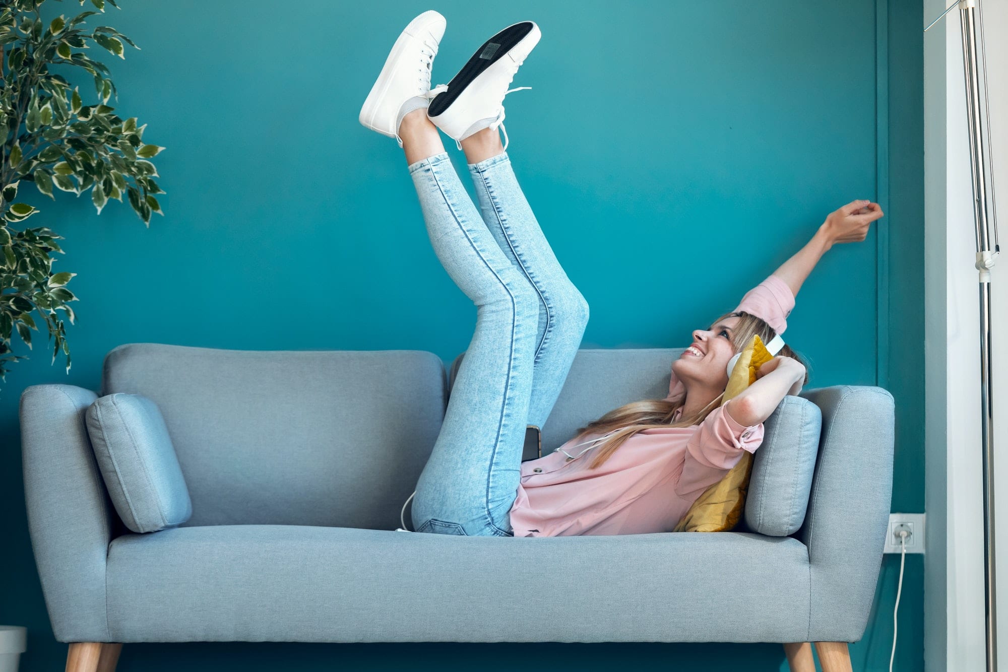 Motivated young woman listening to music with smartphone while lying on sofa at home.