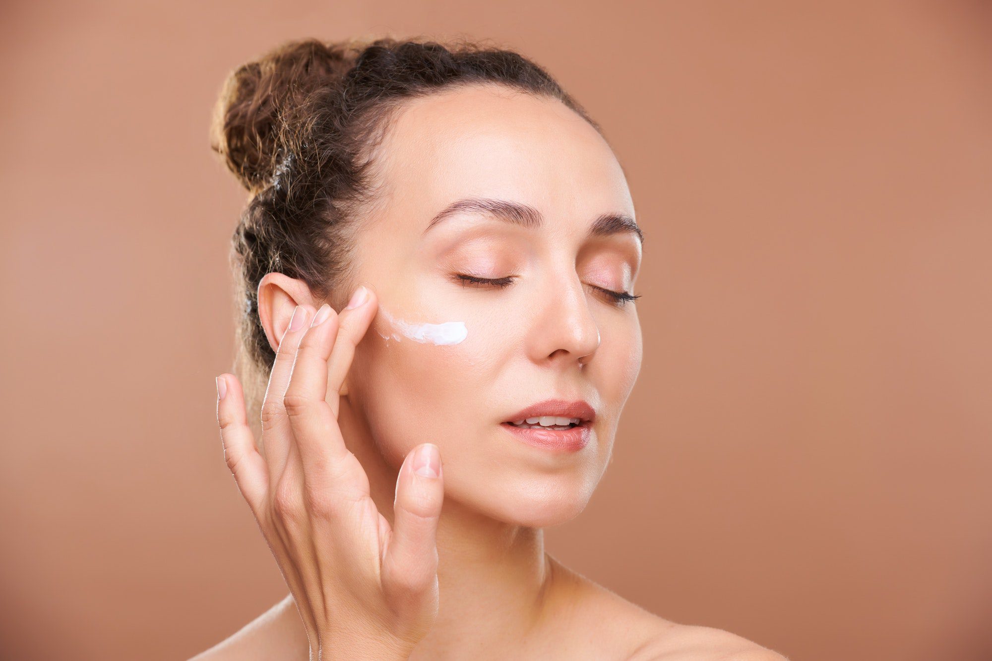 Young gorgeous woman applying facial cream or serum on undereye area