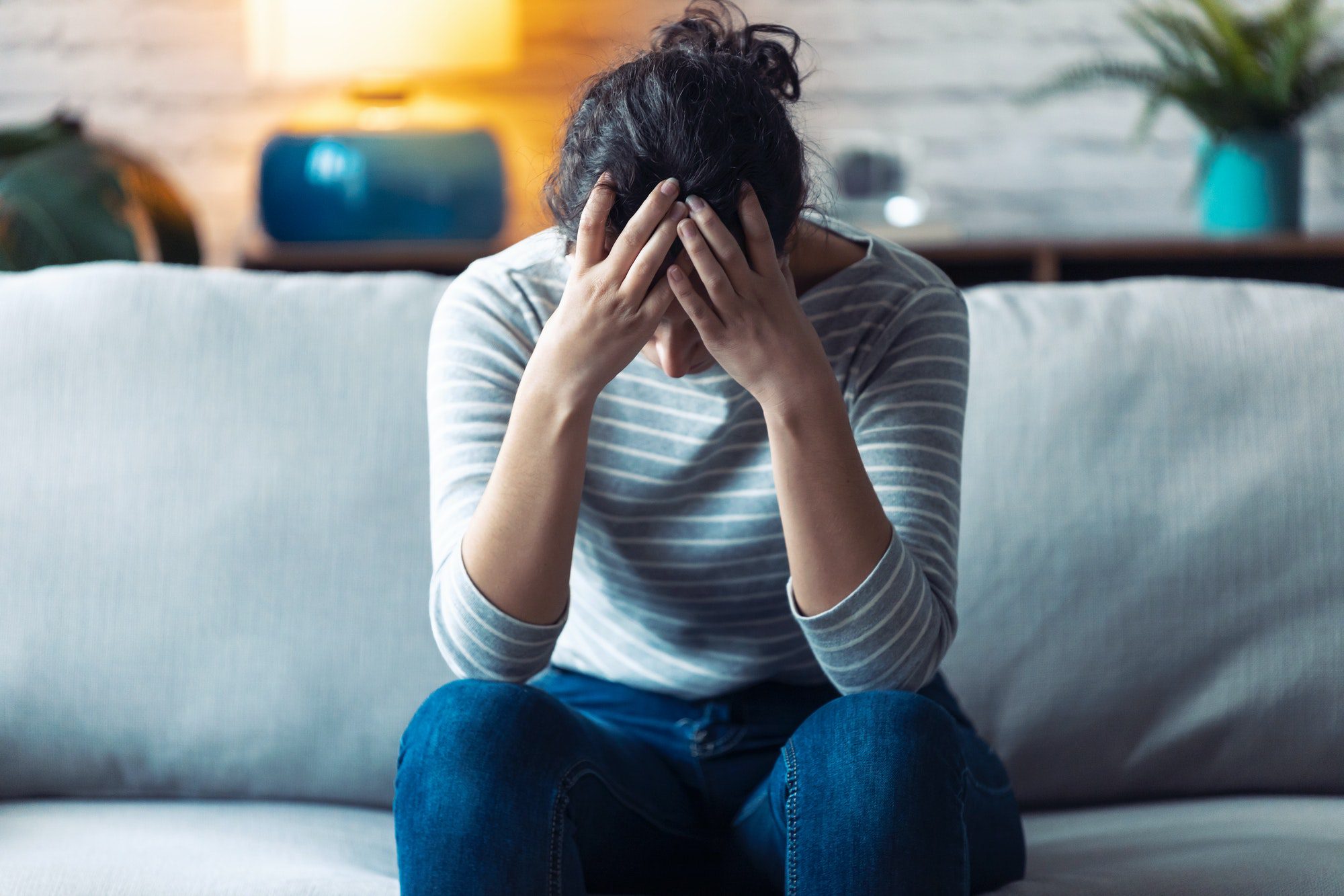 Depressed young woman thinking about her problems while sitting on the sofa at home.