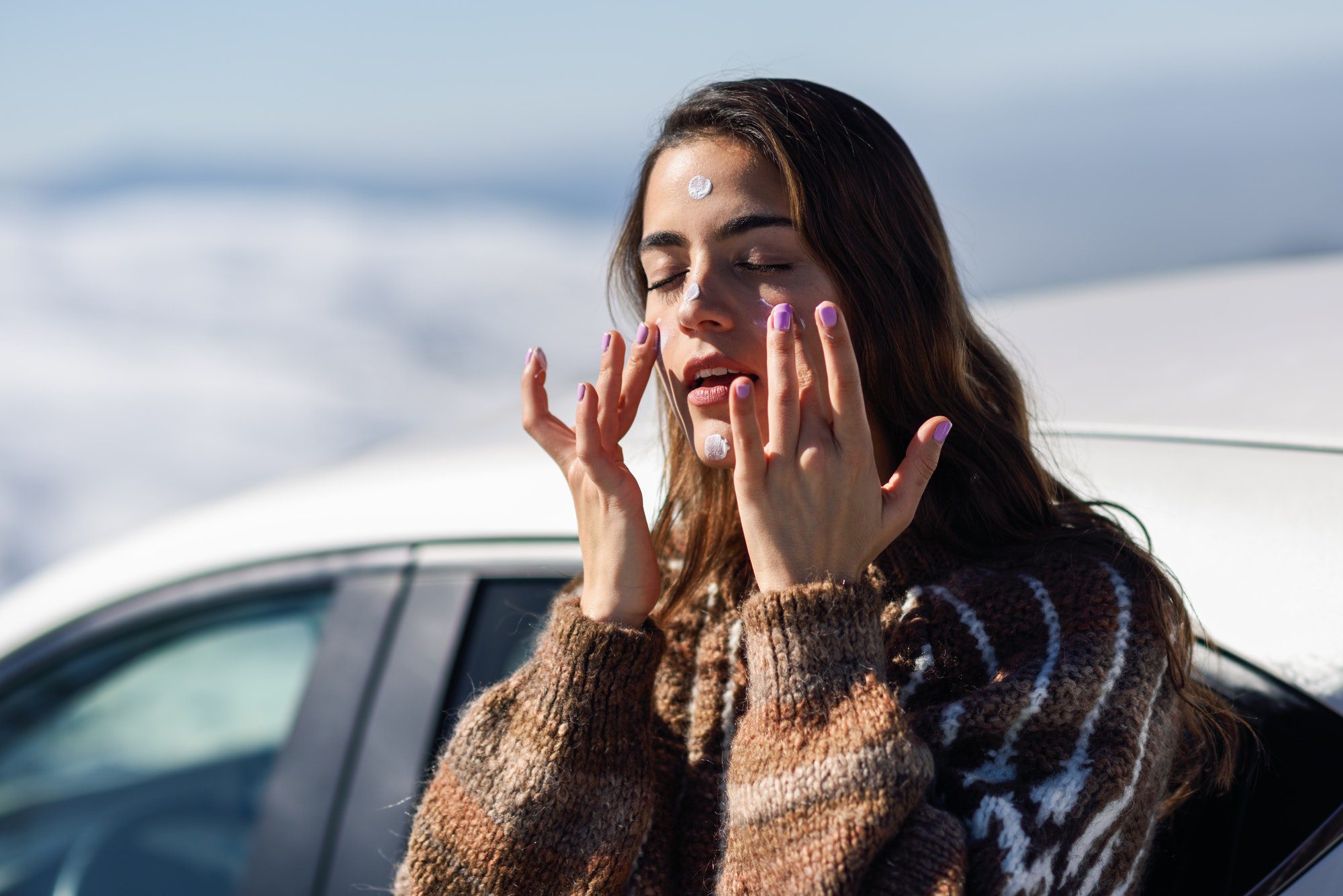 Young woman applying sunscreen on her face in snow landscape