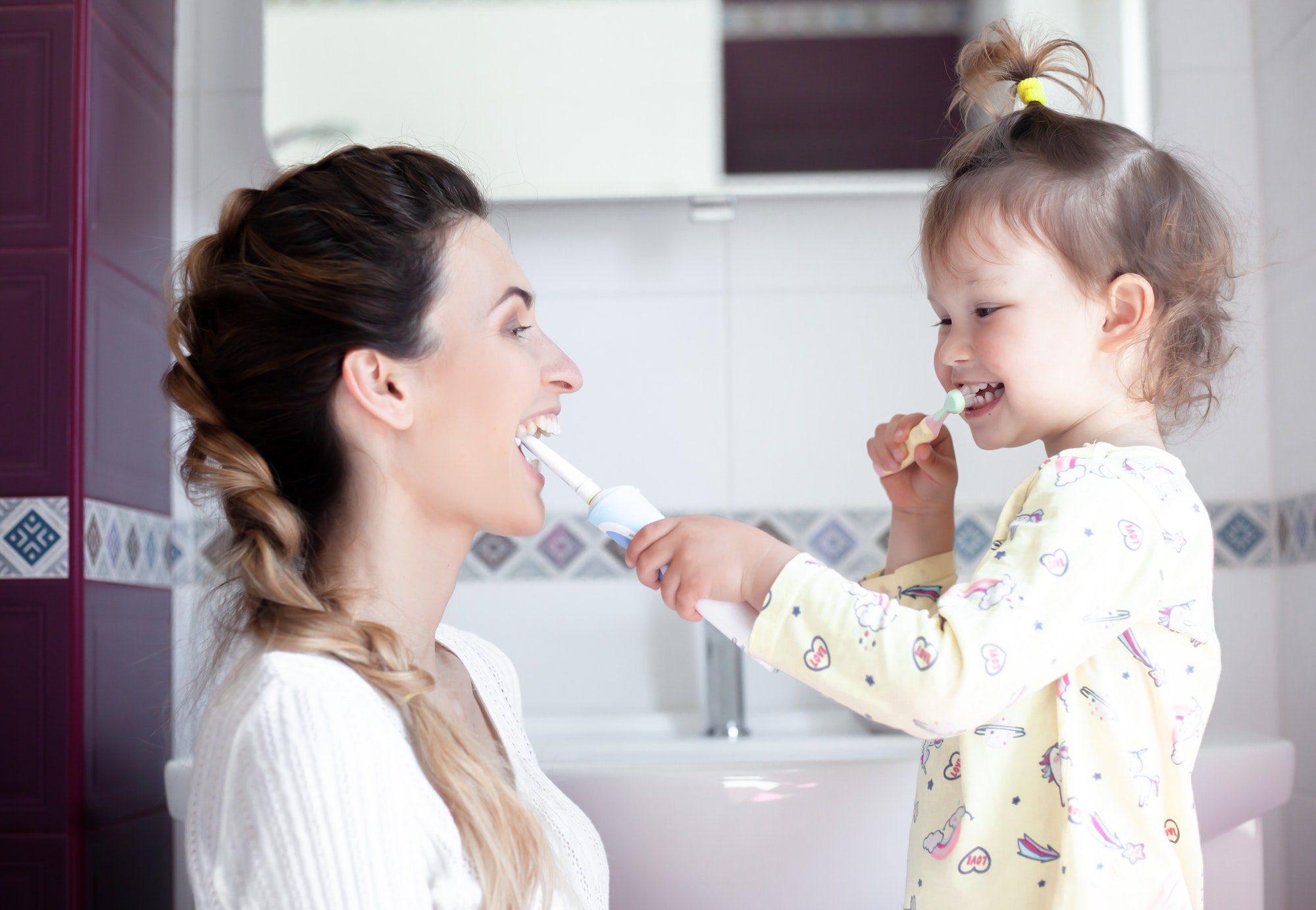 young woman with kid brushing teeth in the bathroom. Woman teaches daughter monitor the health.