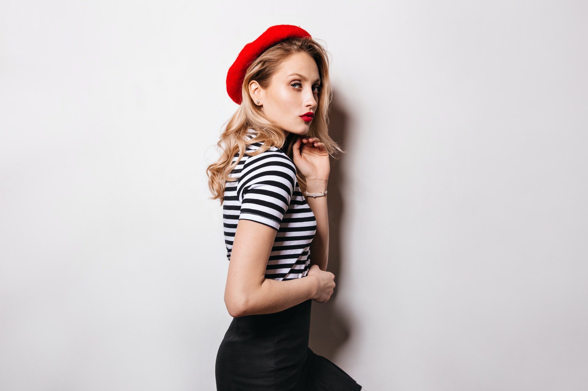 Mysterious blonde girl with red lips looking at camera. Lady in vest and beret posing on isolated b