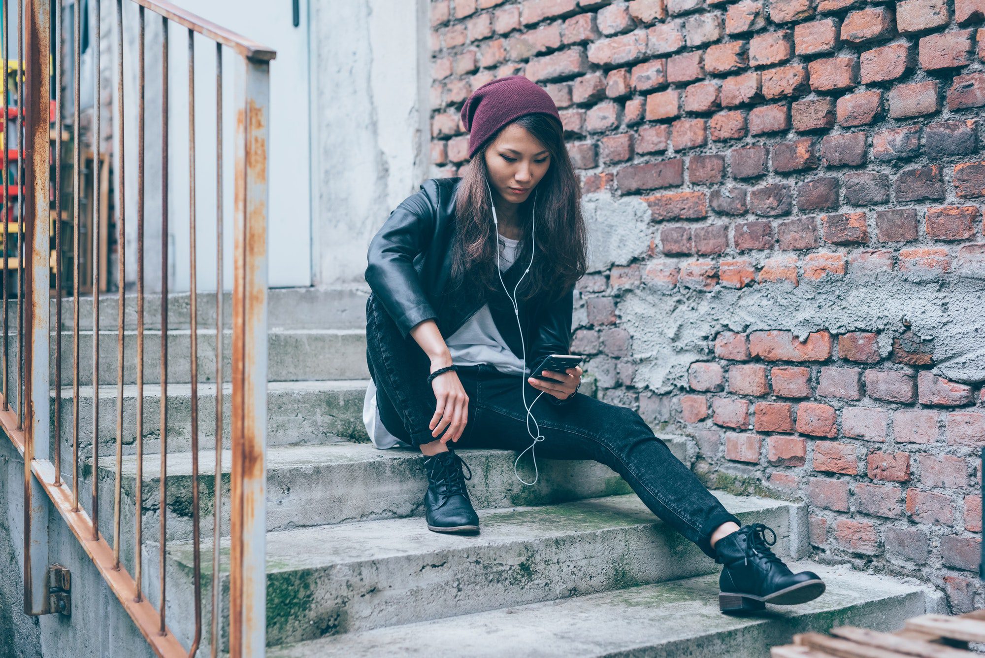 Young beautiful asiatic woman sitting on a staircase listening m