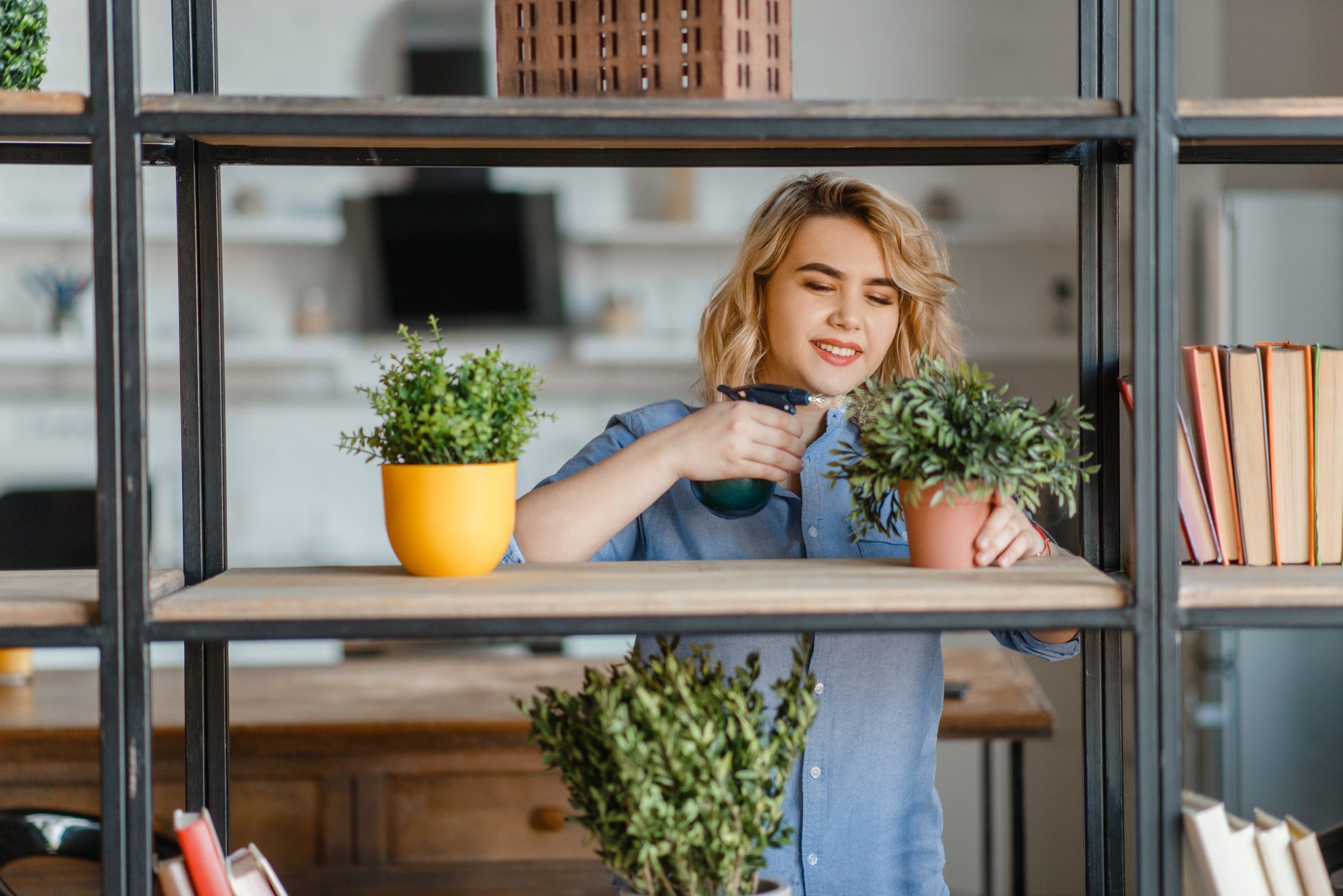 Young woman sprays home plants on the shelf