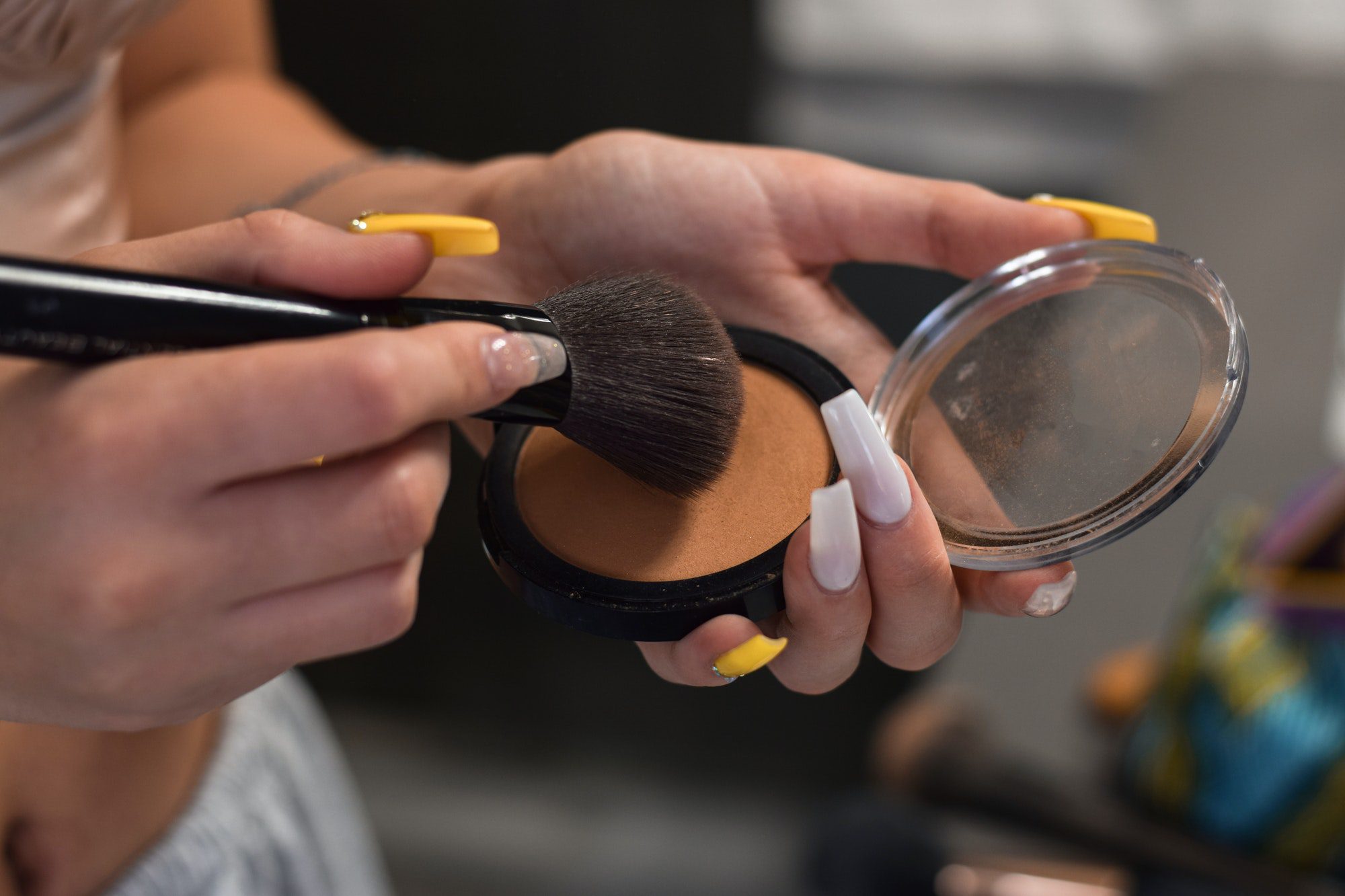 Young woman, teenage girl is using make up brush to apply bronzer, getting ready to go out