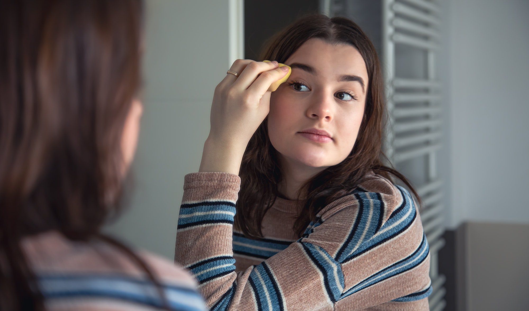 A young woman applies foundation on her face, morning makeup.