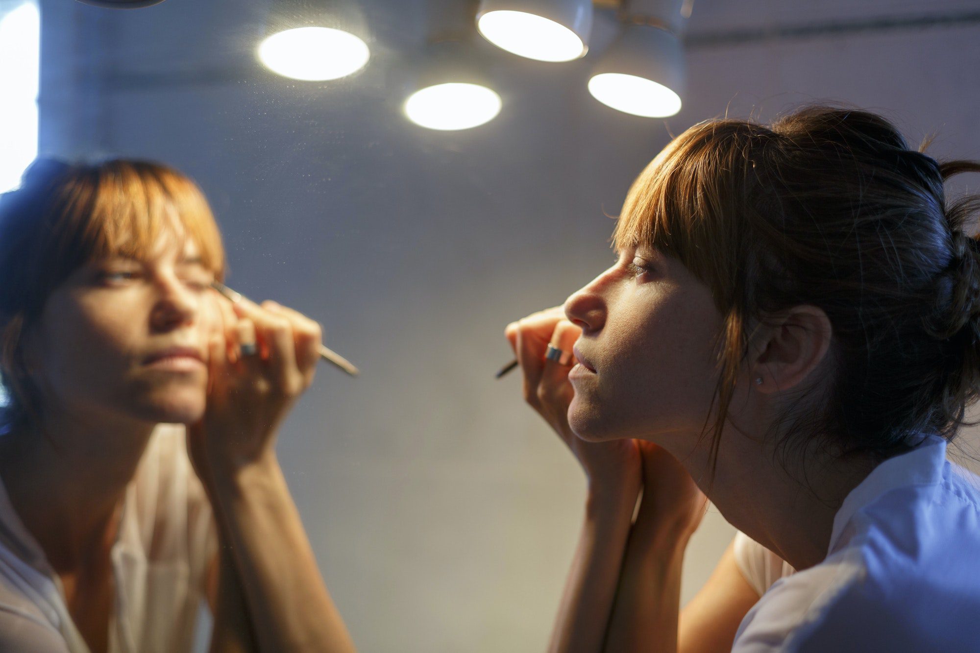 Mid adult woman applying eyeliner in bathroom mirror