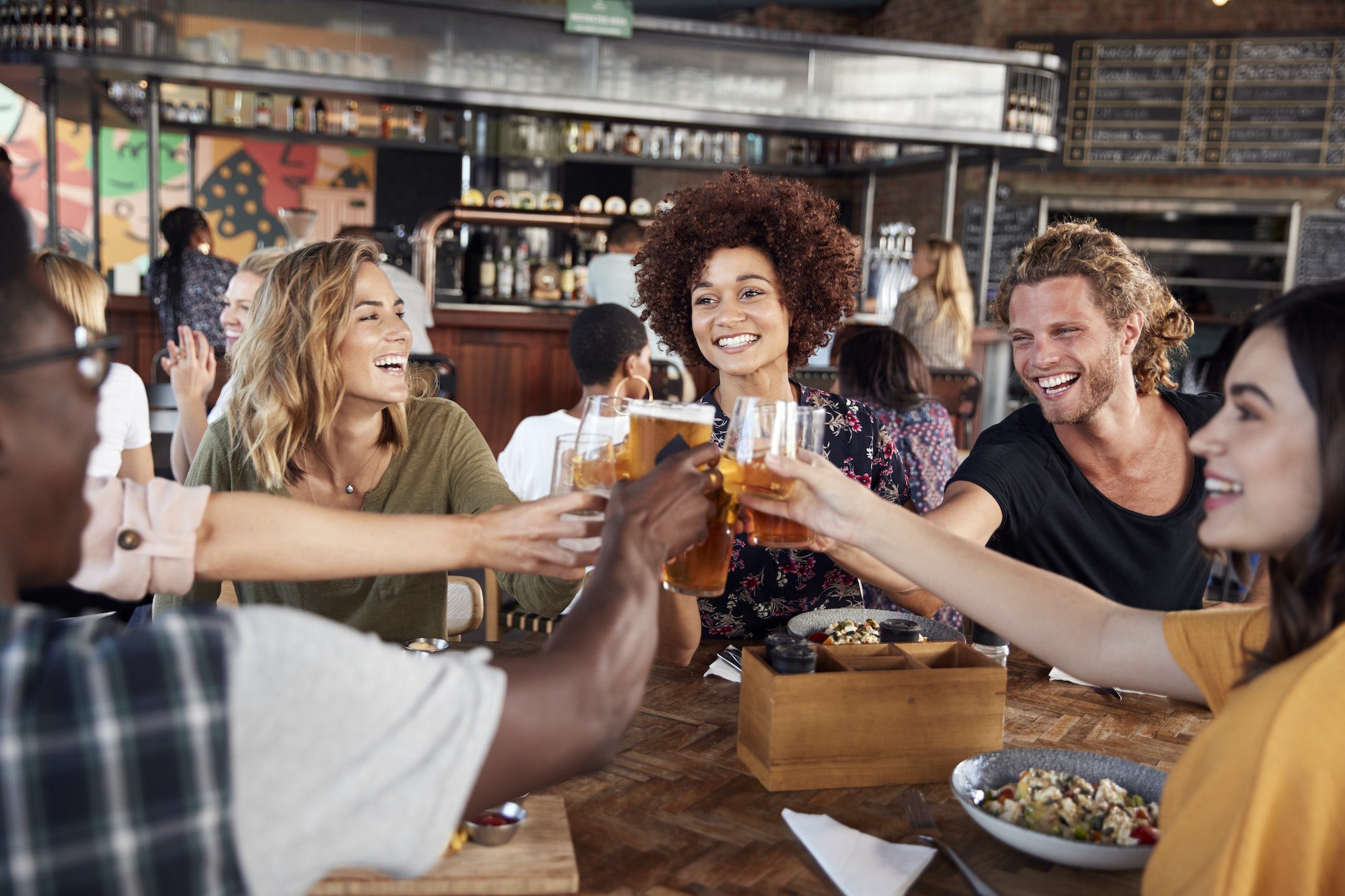 Group Of Young Friends Meeting For Drinks And Food Making A Toast In Restaurant