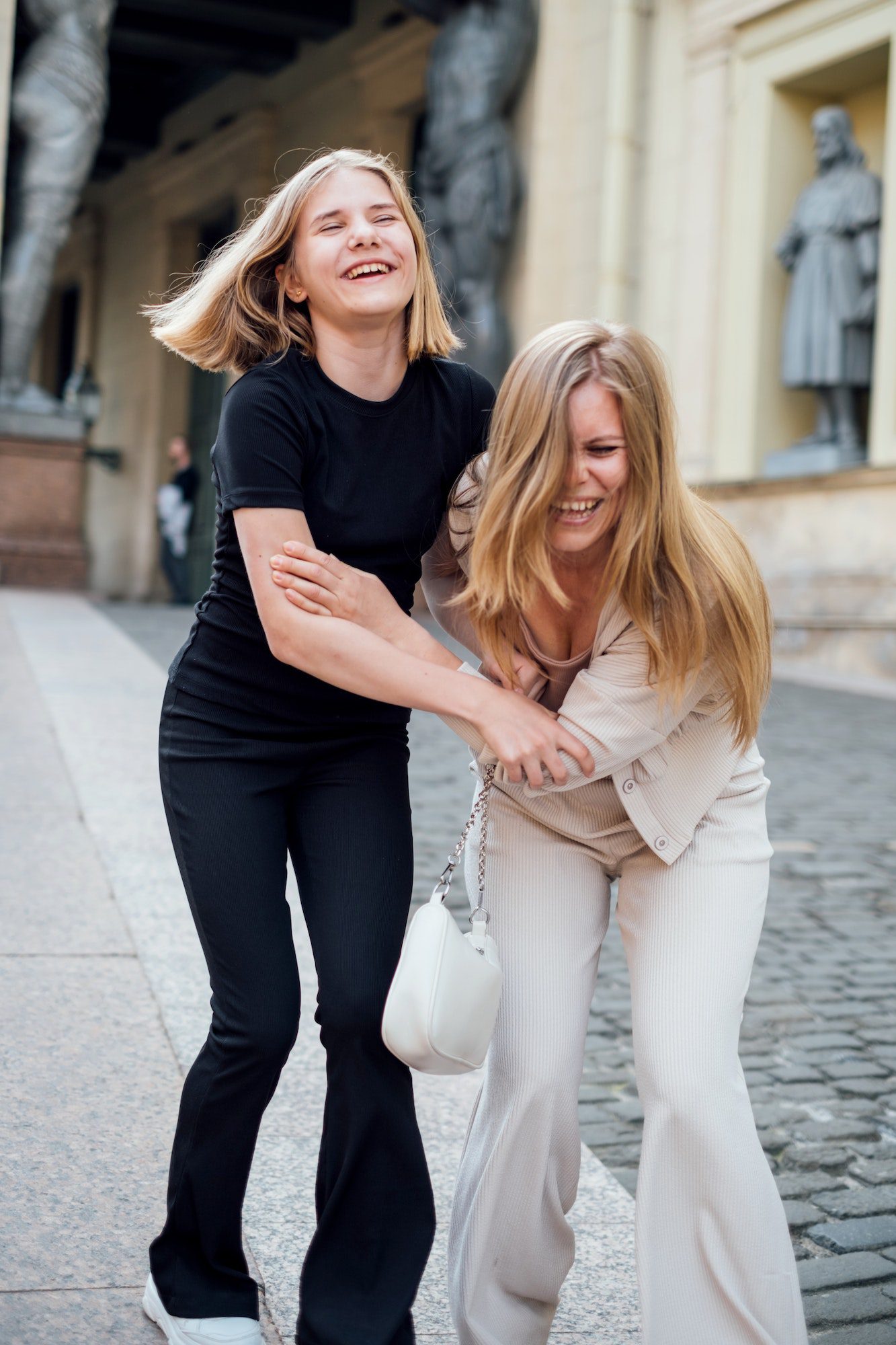 Mom and teenage daughter are walking around the city and laughing merrily.