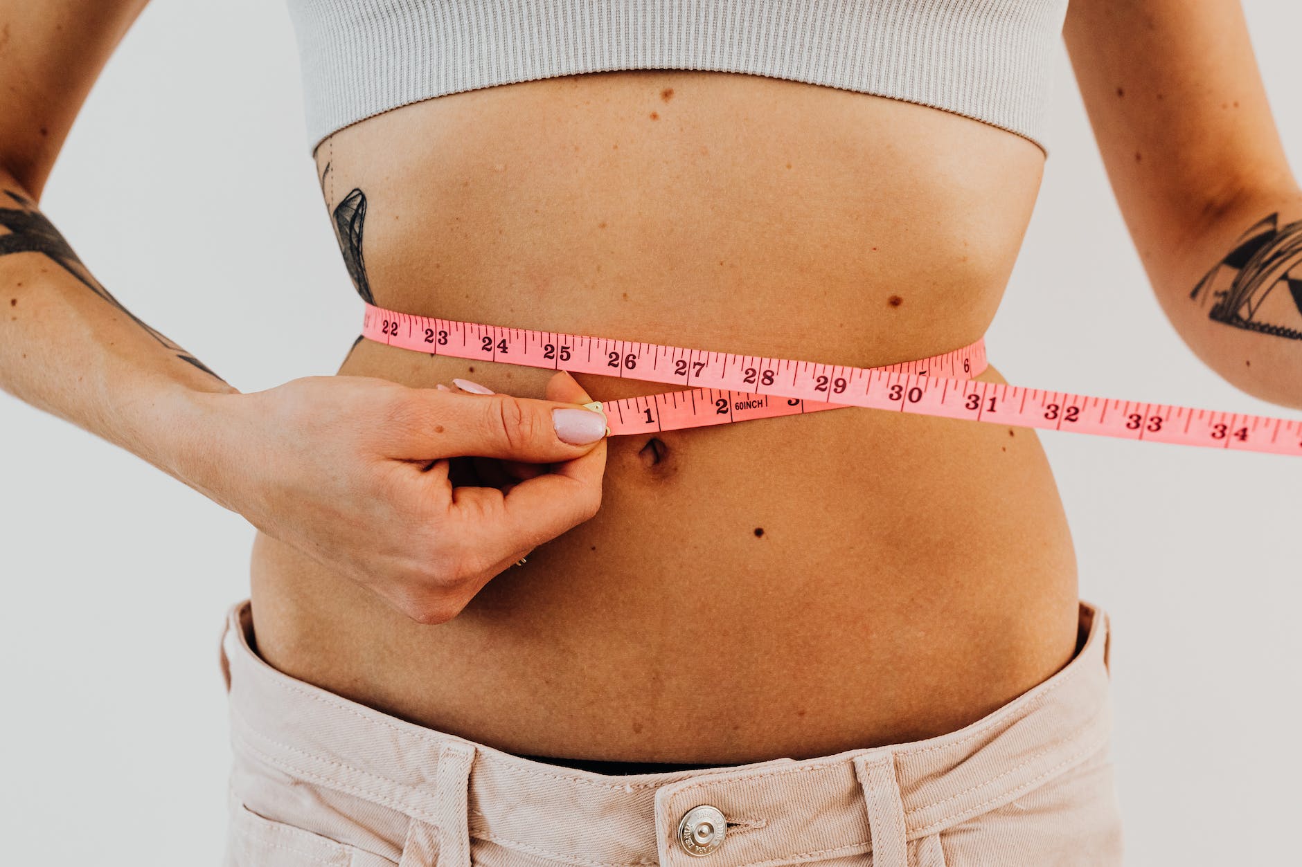 woman measuring waistline with a pink tape measure