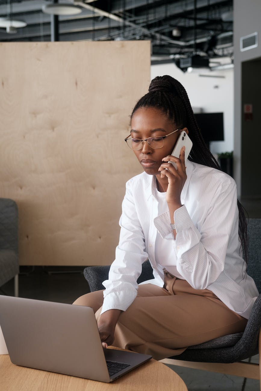 woman using phone while looking at a laptop