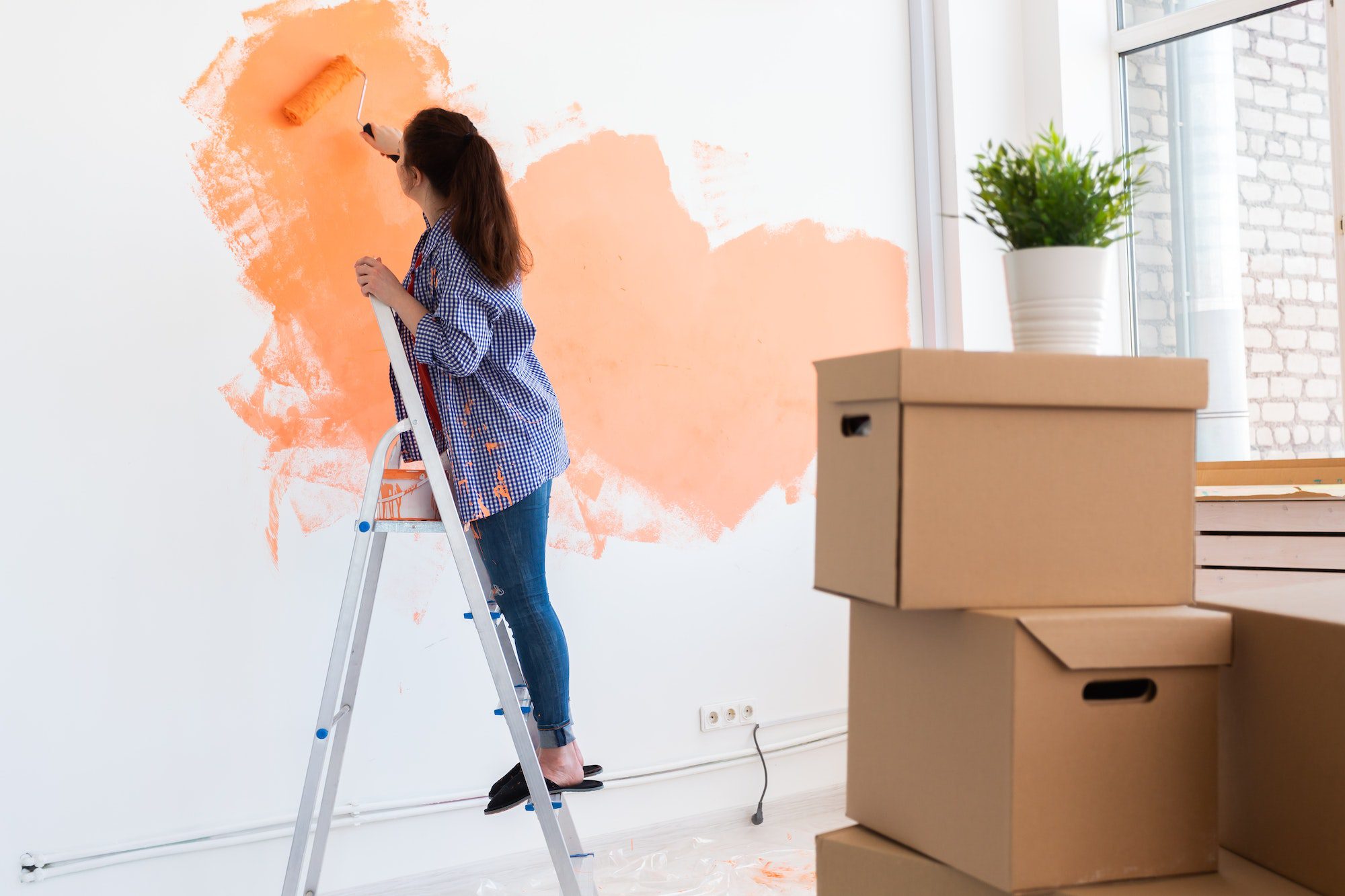 Cheerful woman painting the walls of new home. Renovation, repair and redecoration concept