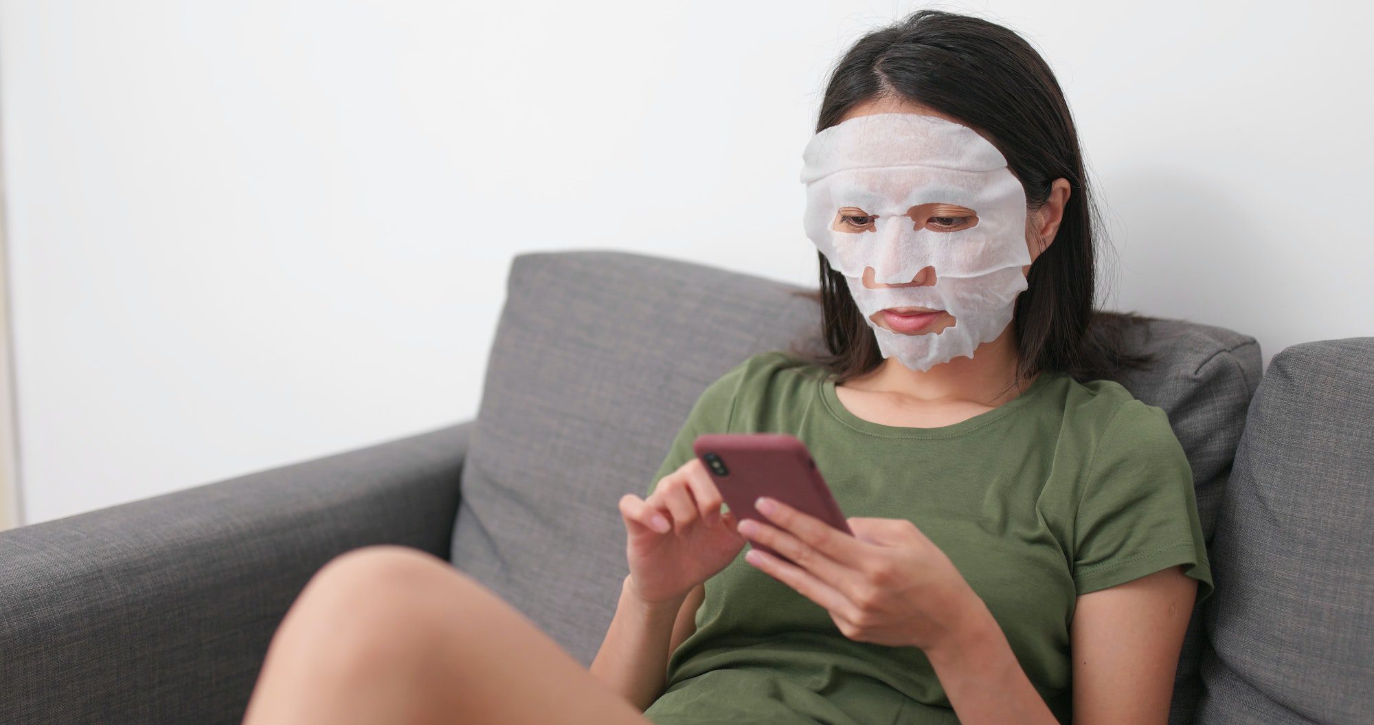 Woman applying skin care paper mask on face and use of mobile phone