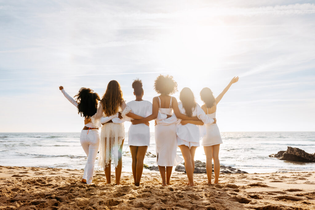 Bride's team. Back view of group of young diverse women posing and embracing by the seashore. Hen